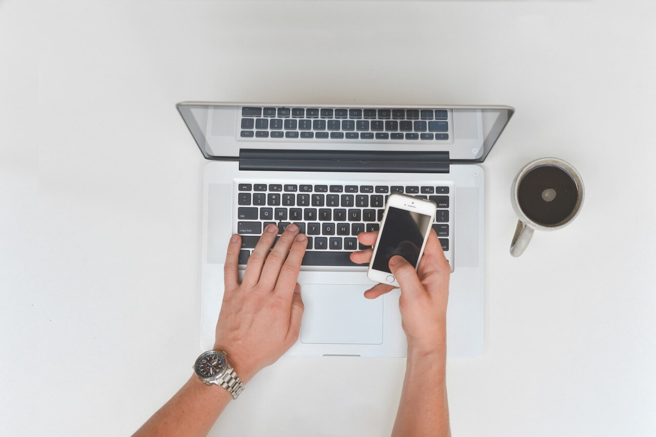 A person in Hong Kong utilizing digital marketing strategies and SEO techniques while working on a laptop and cell phone at a white table.