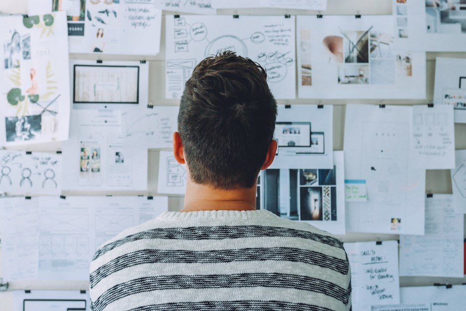 A man stands in front of an award-winning wall full of paper, showcasing his expertise in digital marketing.