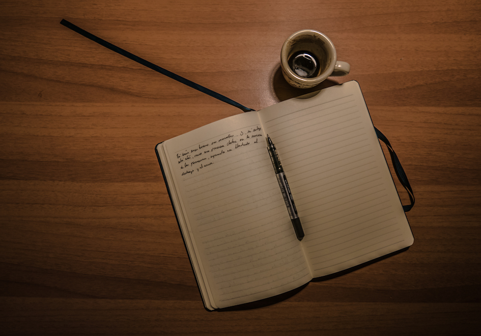 An award-winning digital marketing open notebook with a pen and cup of coffee on a wooden table in Hong Kong.