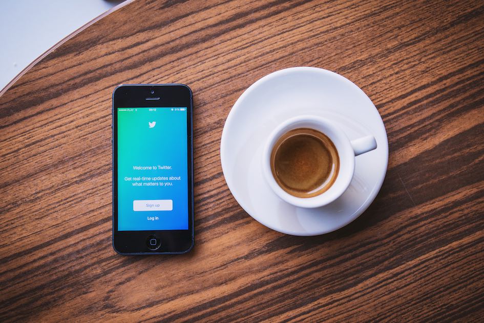 An award-winning smartphone with a Twitter app on it next to a cup of coffee, from Hong Kong.