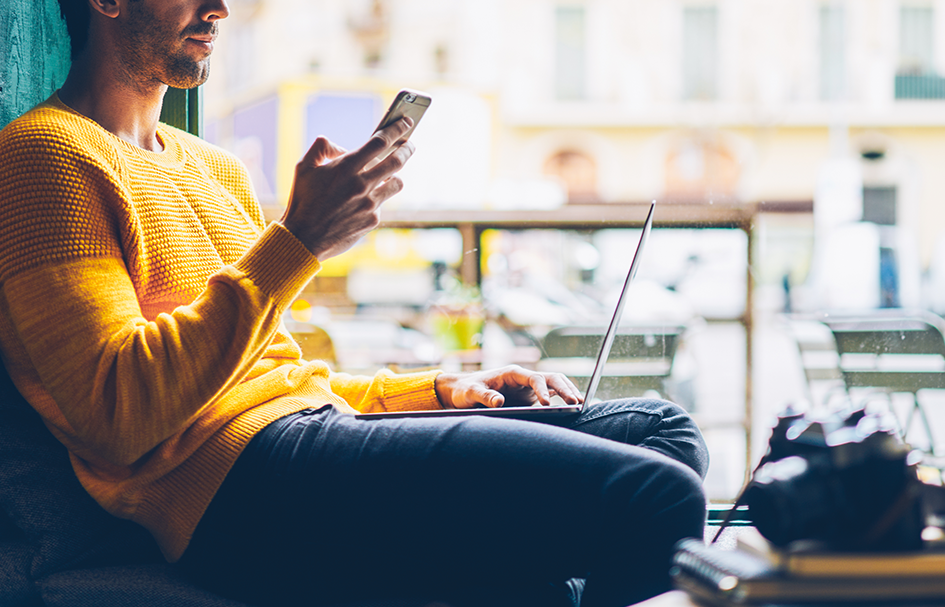 An award-winning man in Hong Kong sitting on a bench with a laptop and cell phone.