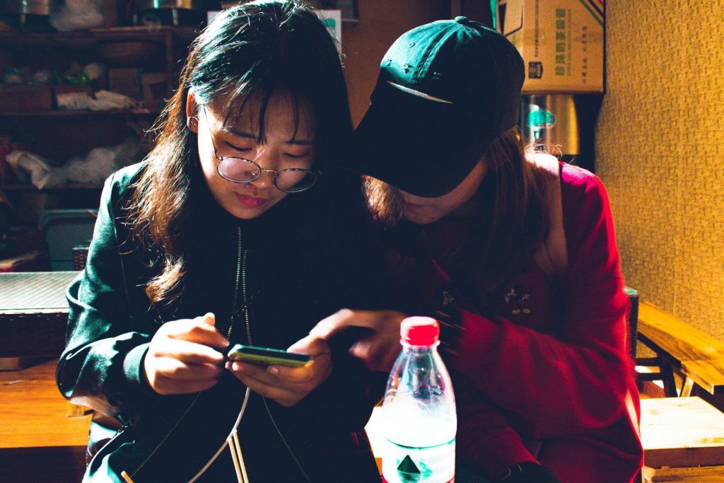 Two award-winning women in Hong Kong are engrossed in digital marketing while looking at a cell phone.